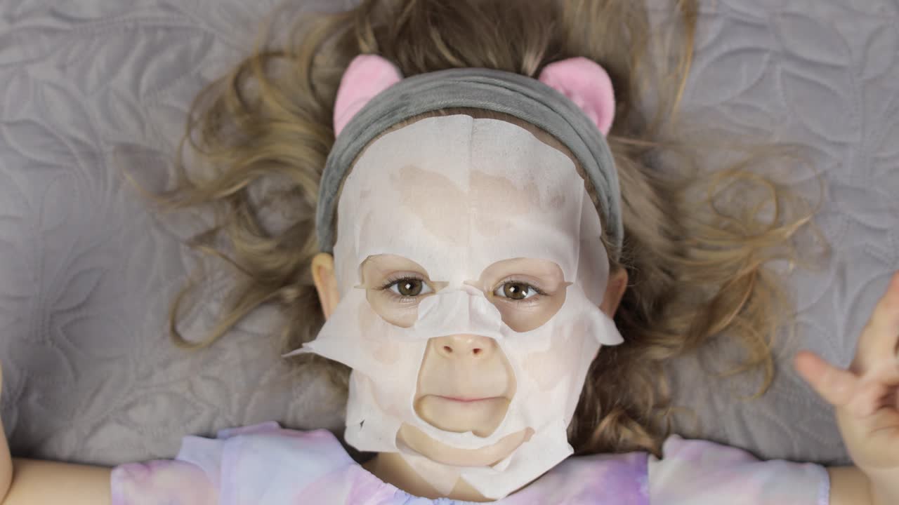 Teen girl applying moisturizing face mask. Child kid take care of skin with cosmetic facial mask