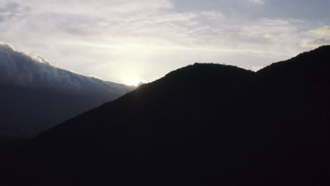 Silueta-De-Ladera-Aérea-Seguimiento-Hacia-Adelante-Revelando-Puesta-De-Sol-Nublada-Y-Montañas-4k