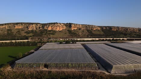 Conjunto-De-Invernaderos-En-El-Lado-De-La-Carretera-Junto-A-Las-Montañas-De-Israel-En-Un-Día-Soleado