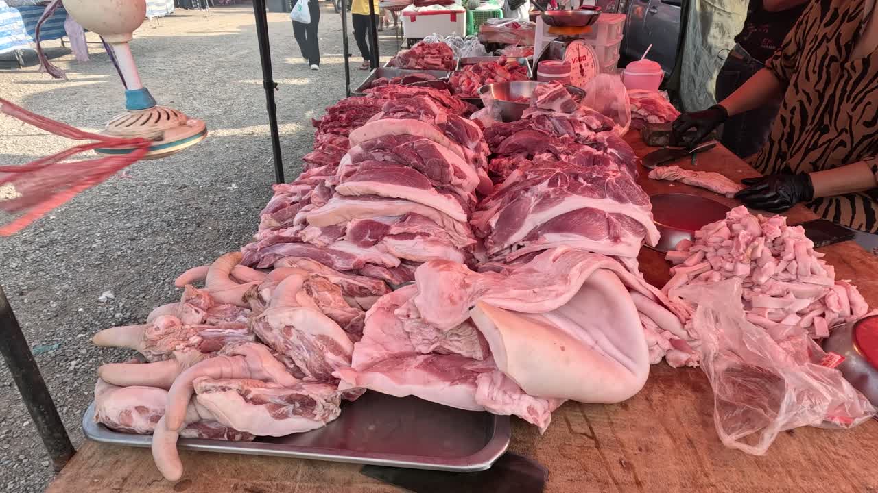 Customers browsing meat at a busy market stall.