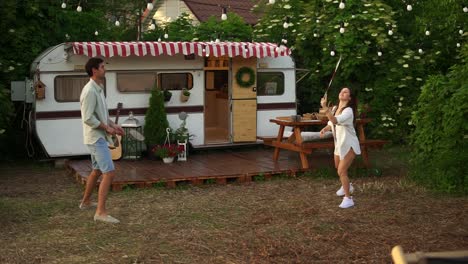 two young tourist couple play badminton next to their trailer in american retro style. active vacation, rest, traveling. summer, warm day