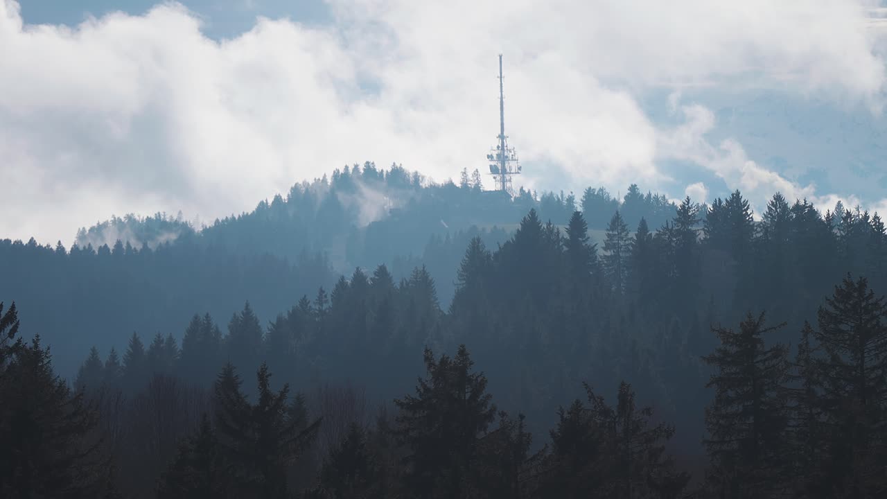 una torre de comunicación con varias antenas unidas se encuentra en la cima de la colina cubierta de bosque en los alpes austriacos