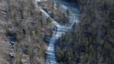 Frozen-River-Through-Forest-Trees-In-The-Mountain-On-A-Sunny-Winter-Day-In-Quebec,-Canada