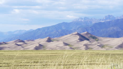 stunning late summer early fall view of the great sand dunes national park colorado rockies mountain sandy 14er peaks crisp golden yellow tall grass wind clouds blue sky mid day cinematic slow motion