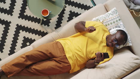 black man in headphones listening to music on smartphone at home
