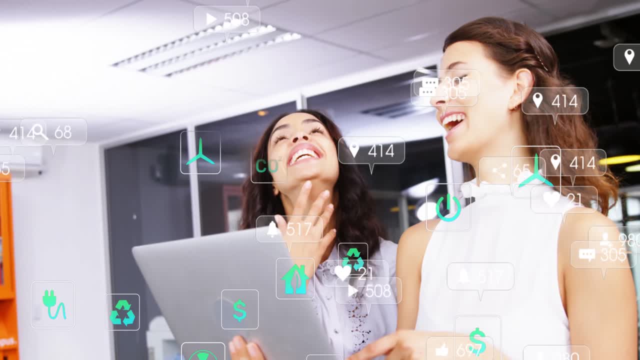 사무실에서 노트북을 사용하는 동안 웃는 두 명의 다양한 여성 위에 떠다니는 소셜 미디어 아이콘의 애니메이션