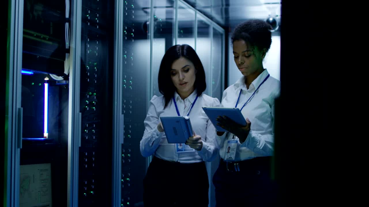 dos mujeres están trabajando en un centro de datos con filas de racks de servidores