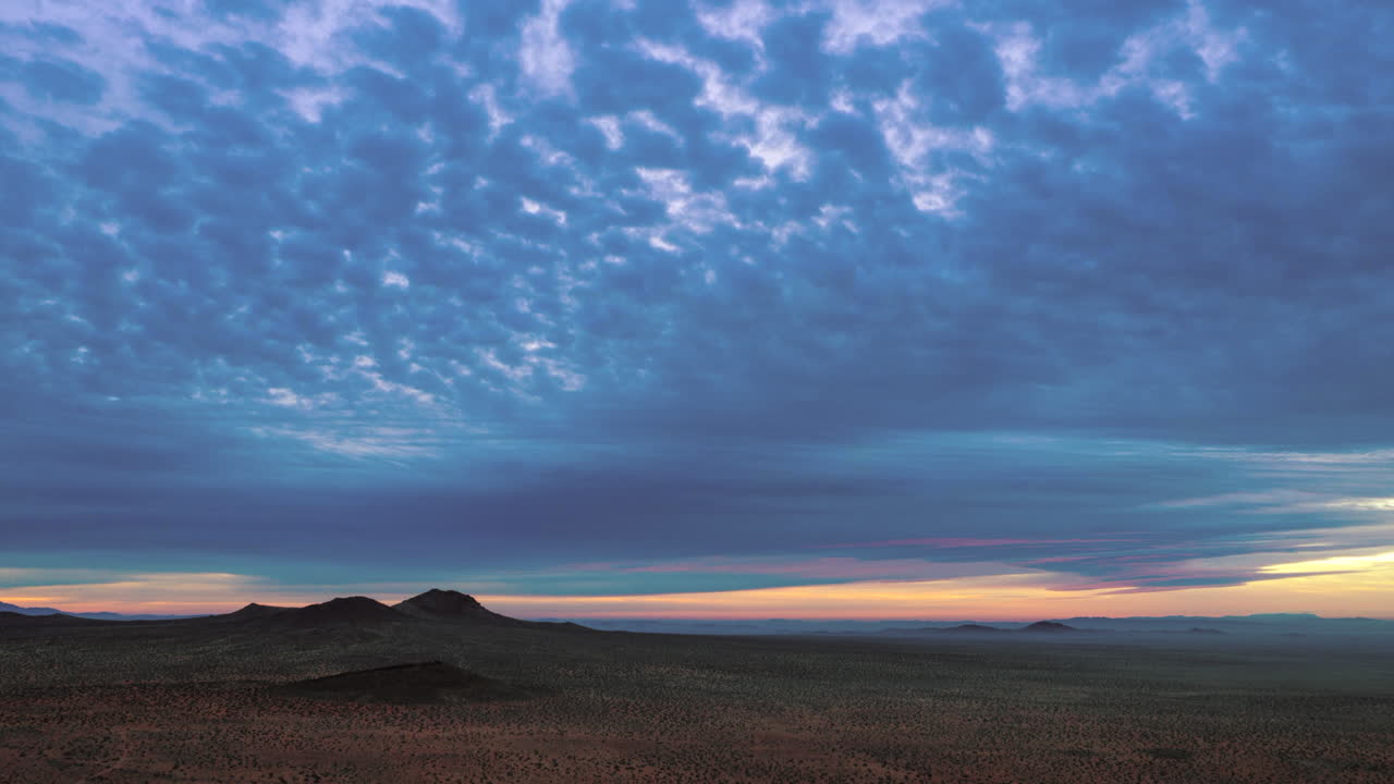 la hermosa y pacífica atmósfera de la puesta de sol sobre una tierra desértica con nubes rodando por encima y una montaña en el fondo - disparo aéreo de lapso de tiempo