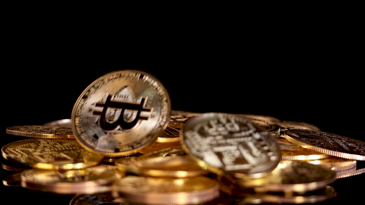 A gold cryptocurrency coin falls onto a pile of coins, dramatic lighting, black background