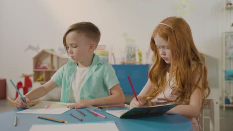 dos niños dibujando con lápices de colores mientras están sentados en el escritorio en la escuela montessori