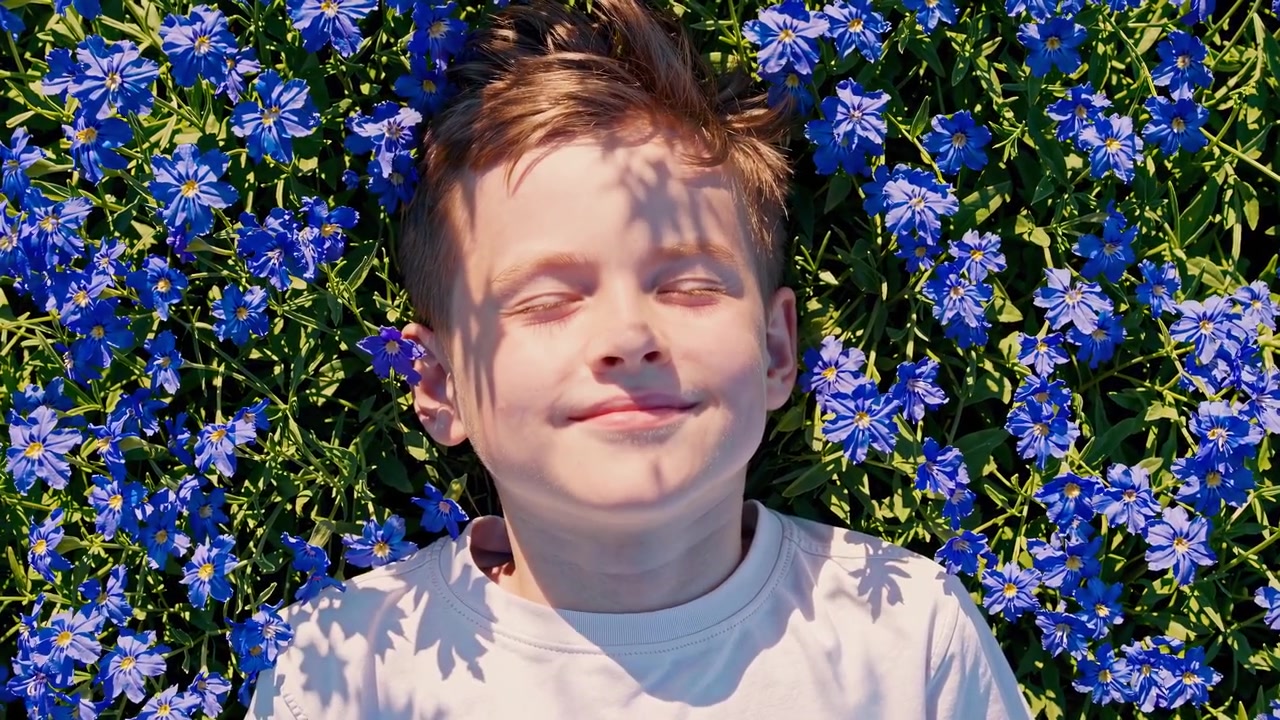 Ung dreng, der slapper af og smiler, mens han ligger i blå blomster.