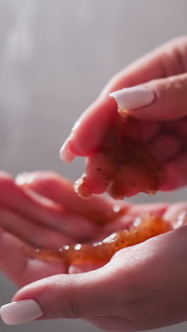 woman shows scrub on palm in shower cabin closeup. lady holds organic cosmetic product for skin exfoliation in bathroom. body care and spa remedy