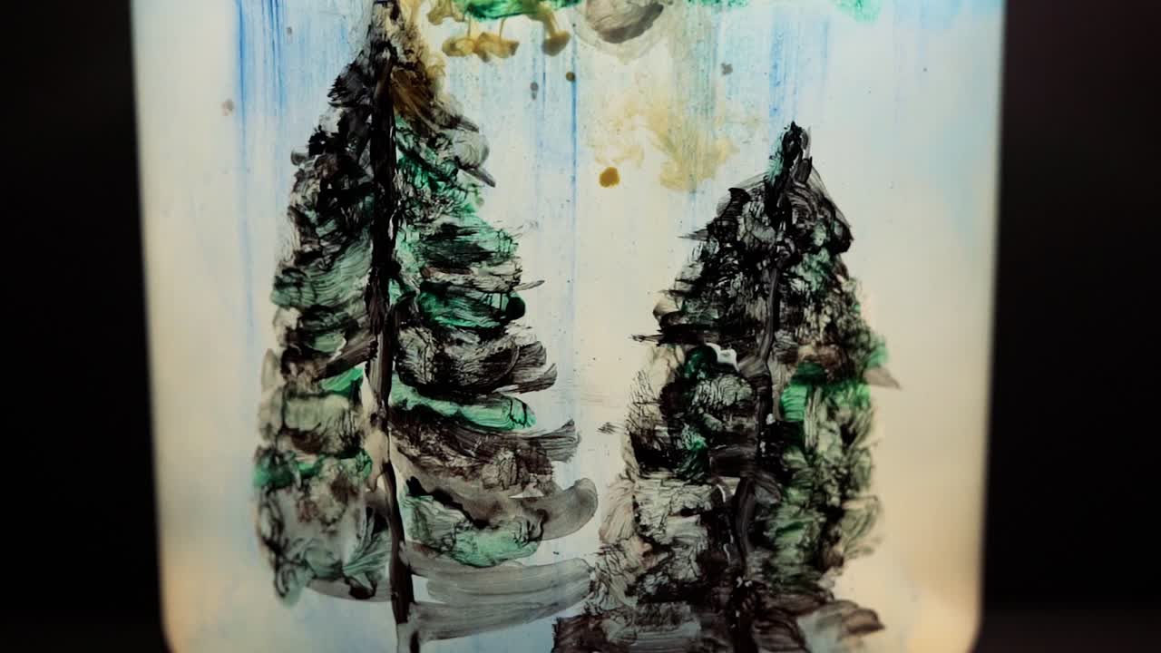 Yellow paint floating in water tank with pine trees drawing inside. Stable shot with the Sony a7iii.