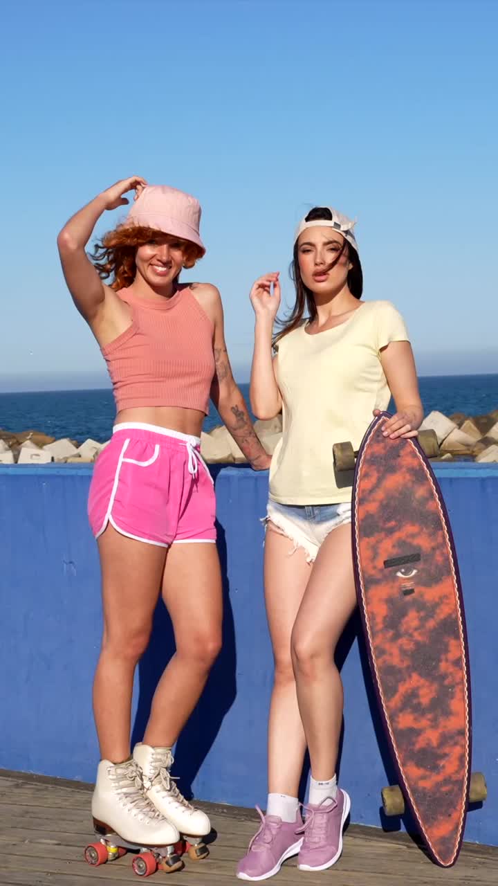 Dos mujeres de pie junto al océano con monopatines