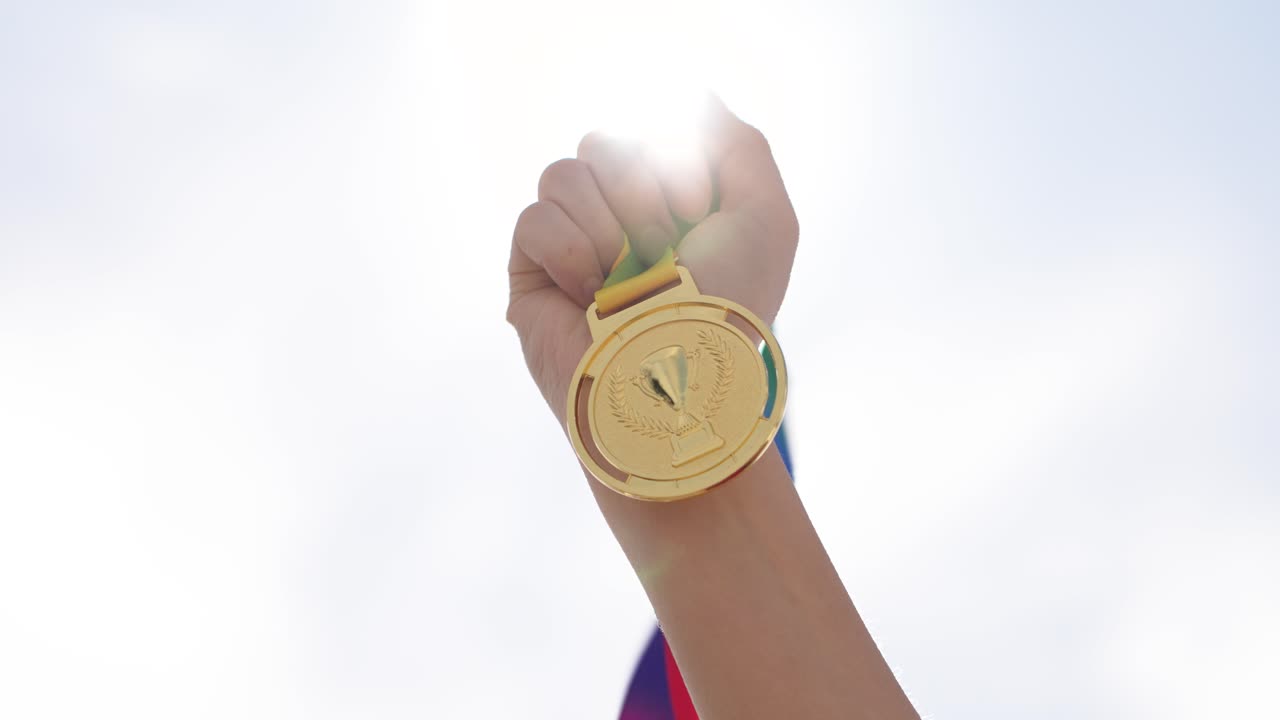 Hand holding gold medal against outdoor sky background. Concept of achievement, success, victory, and motivation. Represents winning, recognition, and reaching goals