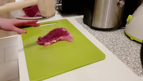 caucasian woman tenderizing pork meat with a white knife on a green board