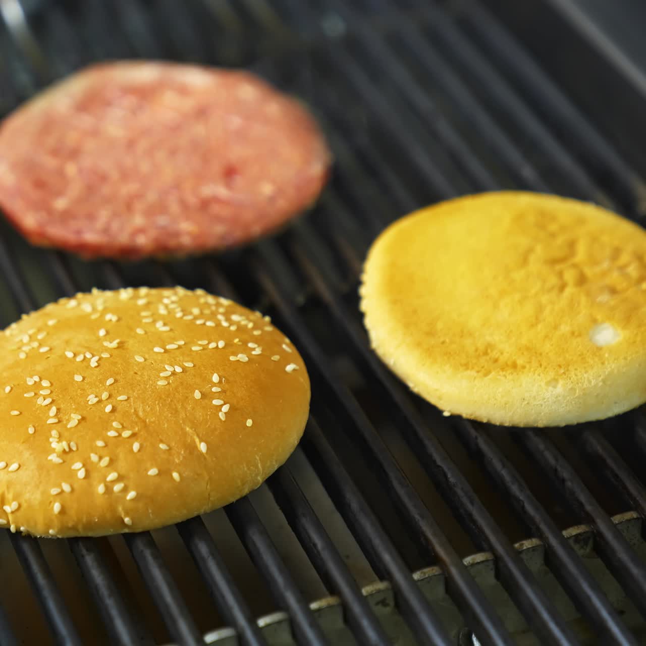 Cooking beef and pork patty for burger. Meat roasted with buns at kitchen grill. Selective video from above