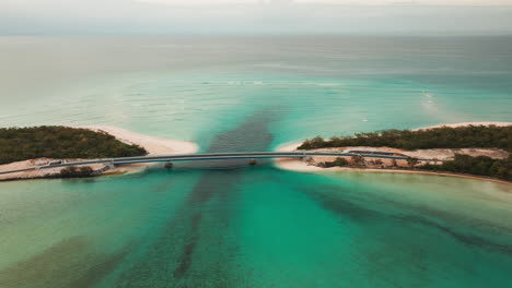 Drone shot of Mouly Bridge crossing the turquoise waters of the Lekini Bay lagoon in Ouvéa, New Caledonia, surrounded by white sandy beaches and shallow reefs