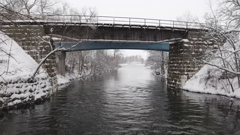 drone shot flying under a small stone road bridge in sweden on a winter day