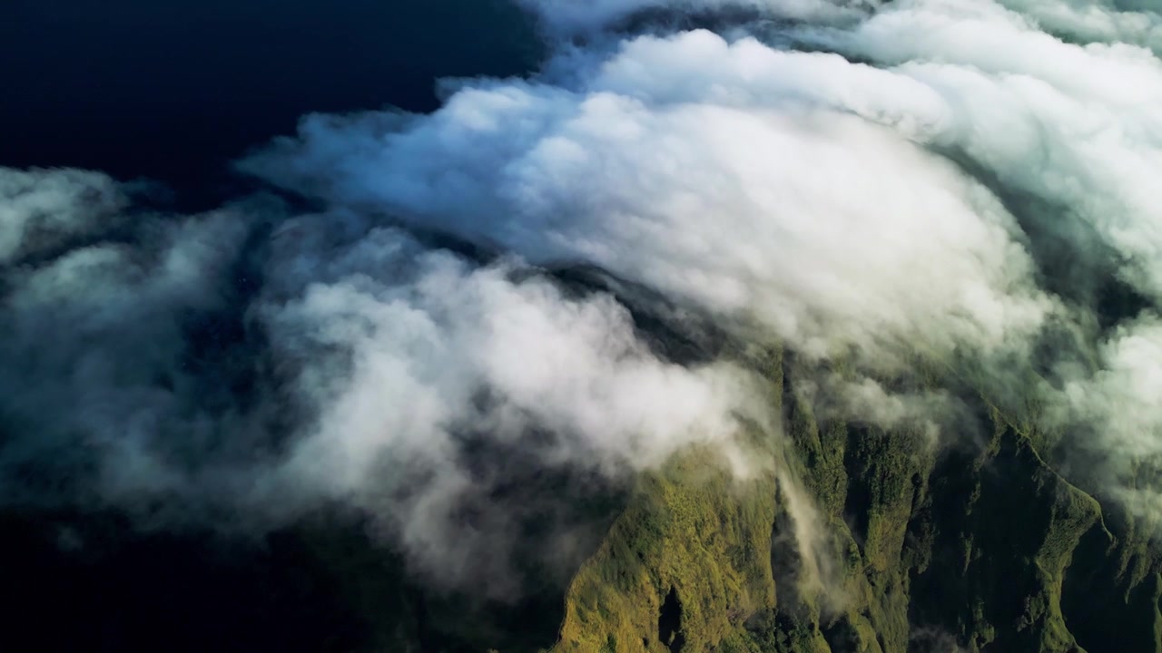 Schnell ziehende Wolken über grünen Berghängen, wobei die Wolkendecke über bewaldete Bergrücken fegt, was eine dramatische atmosphärische Landschaft und eine dynamische Wetterabfolge erzeugt – Drohnenaufnahmen aus der Luft.