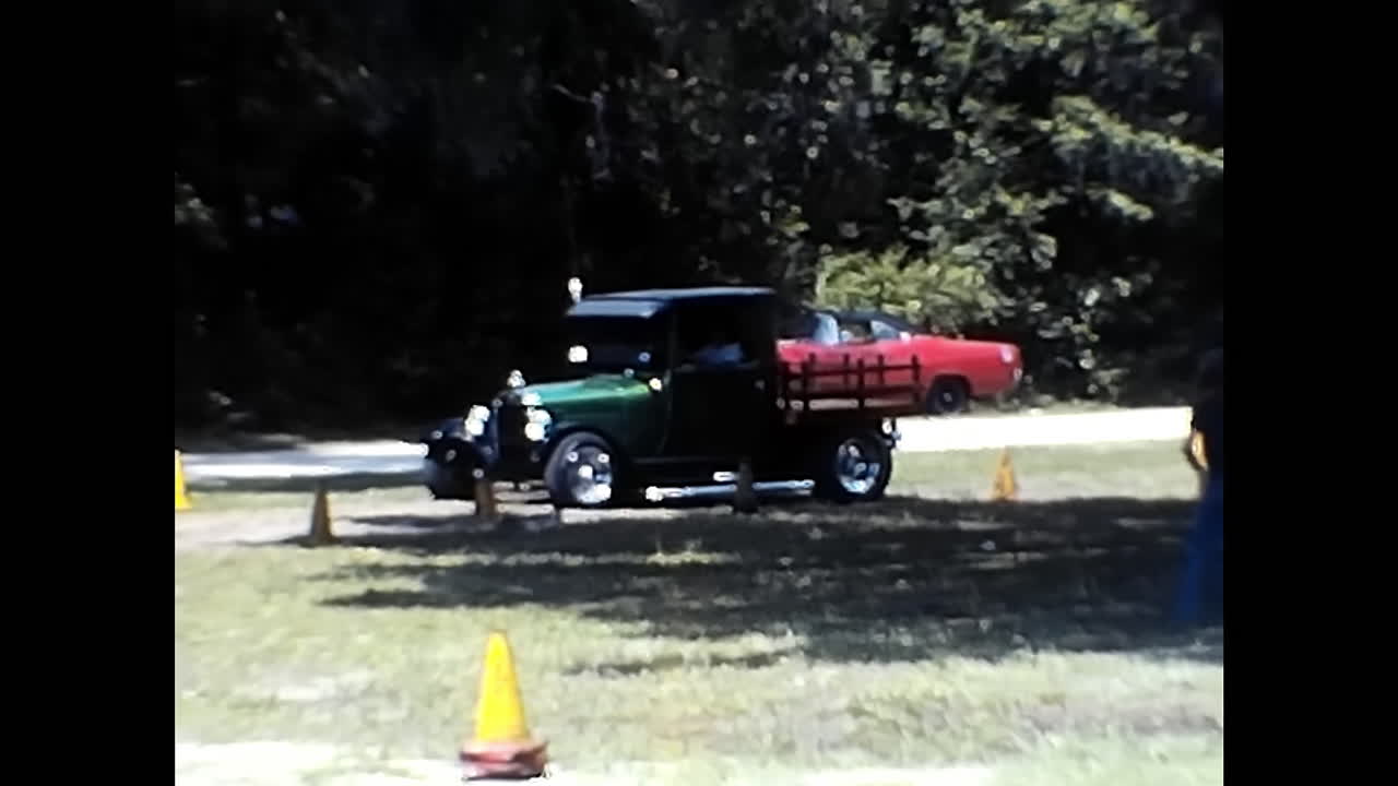 Black Truck Driving Next to Yellow Cones on a Road at an Old Car Show in the 1970s in the USA. CIRCA USA - 1970s: An old black truck gracefully drives down a road lined with vibrant yellow cones at a 1970s car show in the United States.