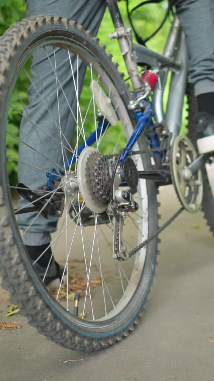 누가 자전거를 타고 오른발로 페달을 고 울창한 초록색으로 둘러싸인 포장된 길에서 은 잎이 바닥에 어져있는 클로즈업