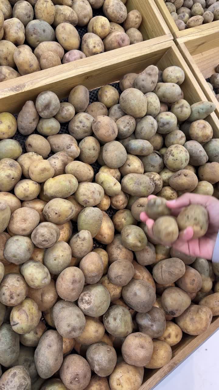 Mano che seleziona patate fresche da una cassa di legno al mercato