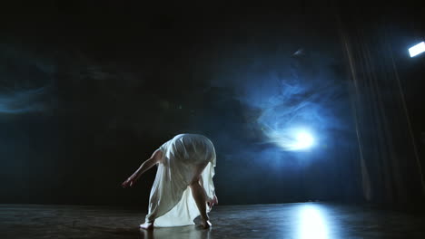 elegant ballerina jumping and dancing in barefoot and white loose oversize dress in studio. with smoke