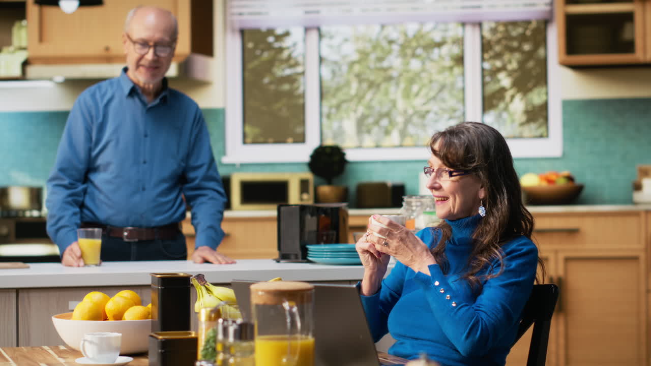 Married people chatting and checking news on laptop together in the kitchen