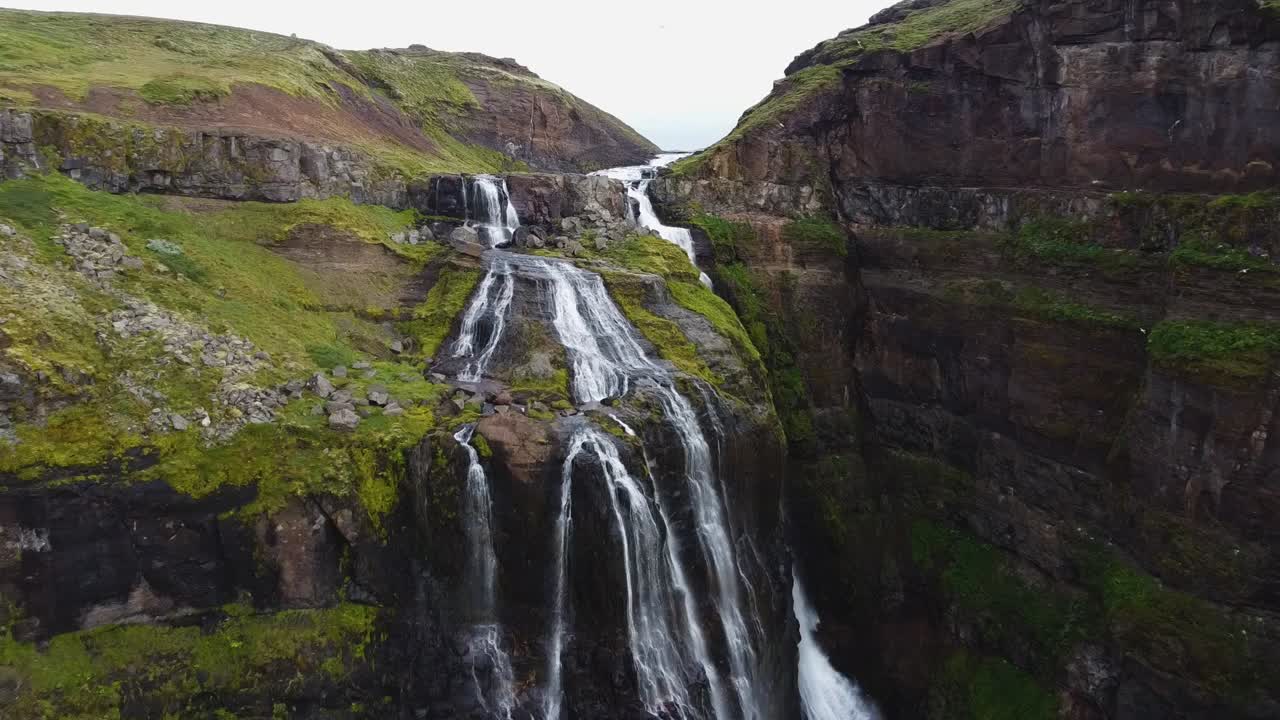 río de montaña que fluye entre acantilados cubiertos de musgo, vista frontal de la cascada de glymur, islandia