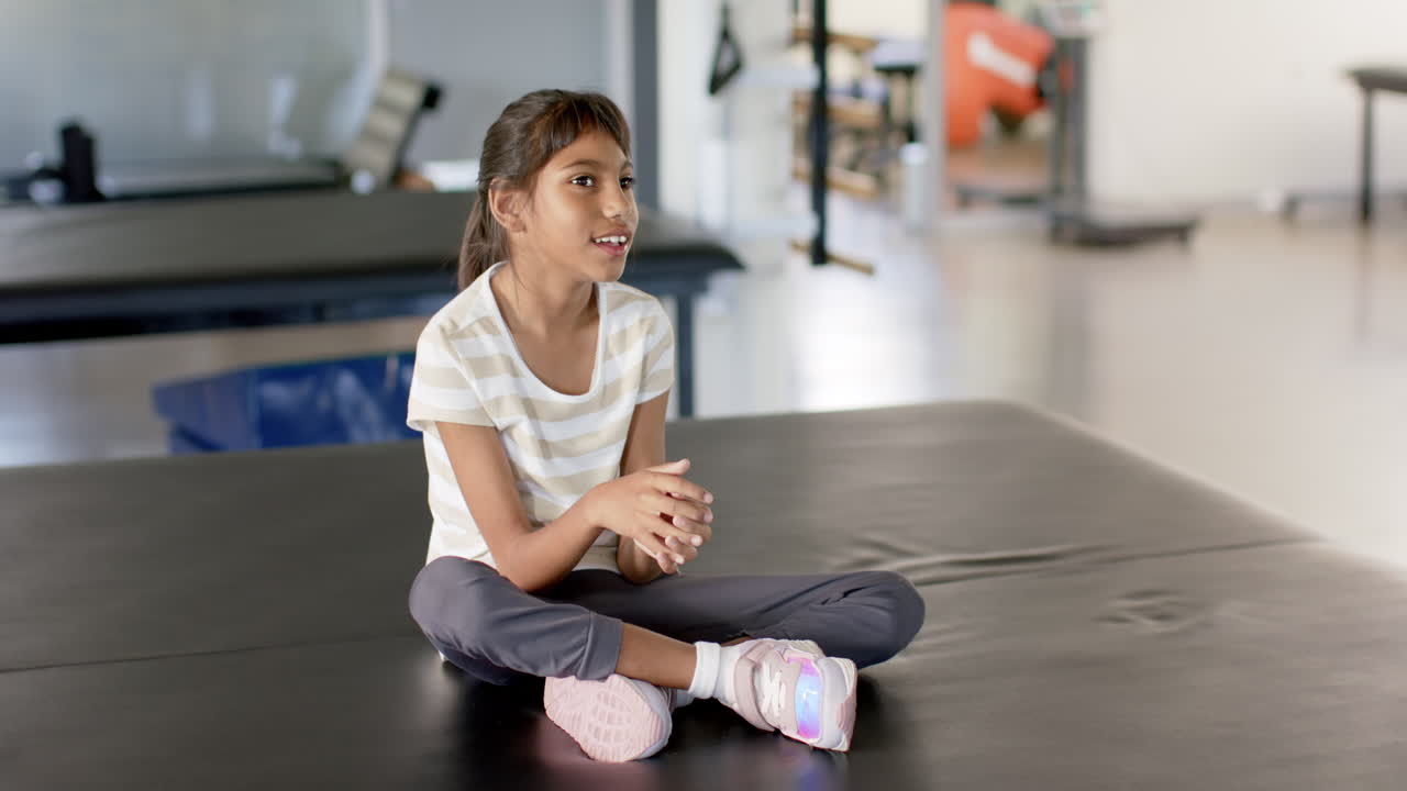 Smiling during disability rehabilitation session, girl with cerebral palsy sitting on therapy table