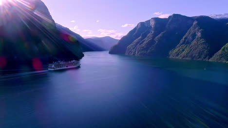 aerial view of cruise ship sailing through dreamy fjord with sun flares hitting lens