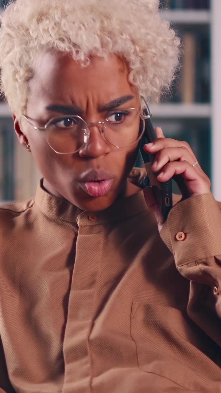 African american woman in glasses having serious phone conversation in library