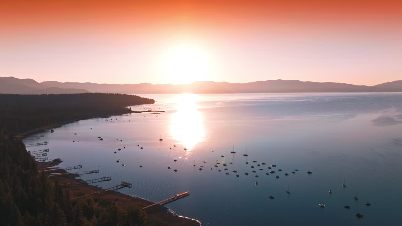 Amazing scenery of Lake Tahoe with numerous boats on. Forest waterfront and sun reflecting in the smooth surface of water. Pink skies at backdrop.