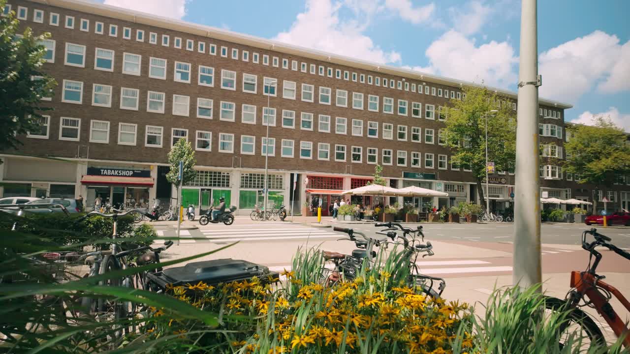 Urban street scene with a long building, storefronts, and many bicycles parked in the foreground.