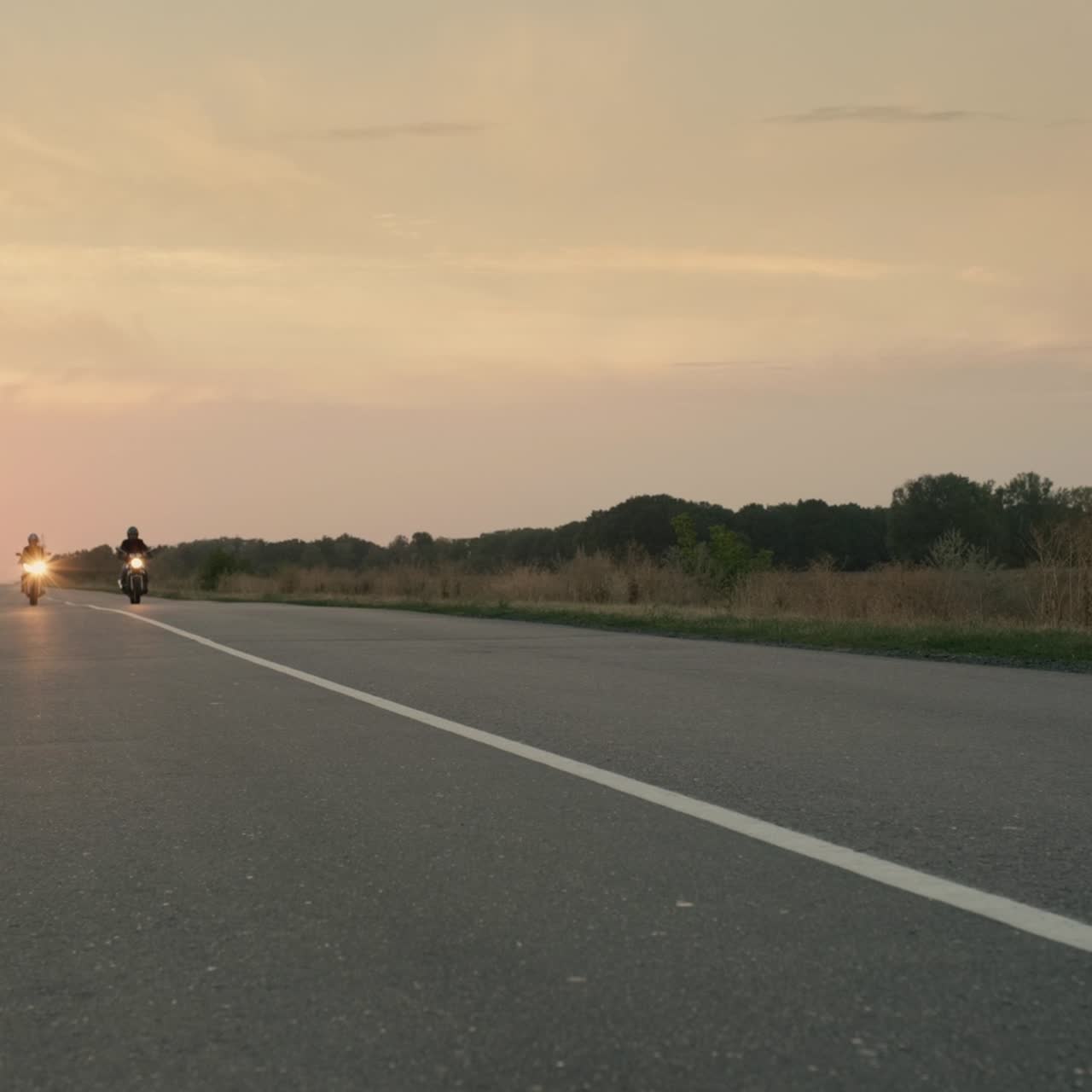 세 명의 오토바이 운전자가 해가 질 때 고속도로를 따라 운전합니다.
