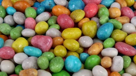 pile of many round chewy candies dragee in multicolored glaze rotate slowly on turntable.