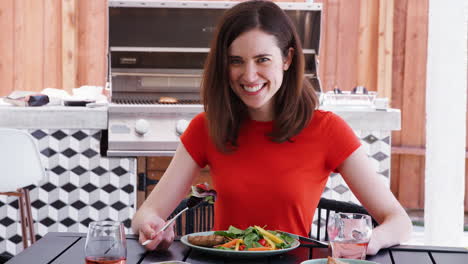 Young-white-woman-eating-lunch-at-a-table-in-teh-garden