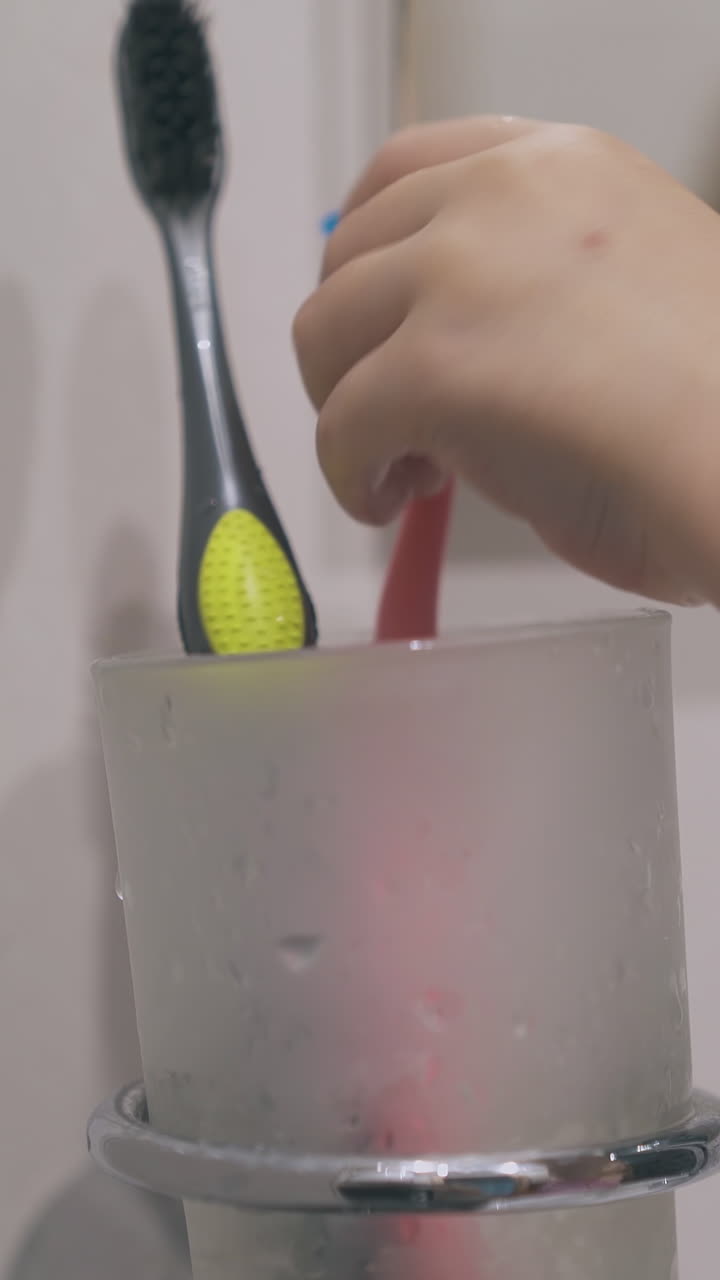 funny little girl puts pink toothbrush into glass holder at mirror in modern bathroom closeup focus on hand