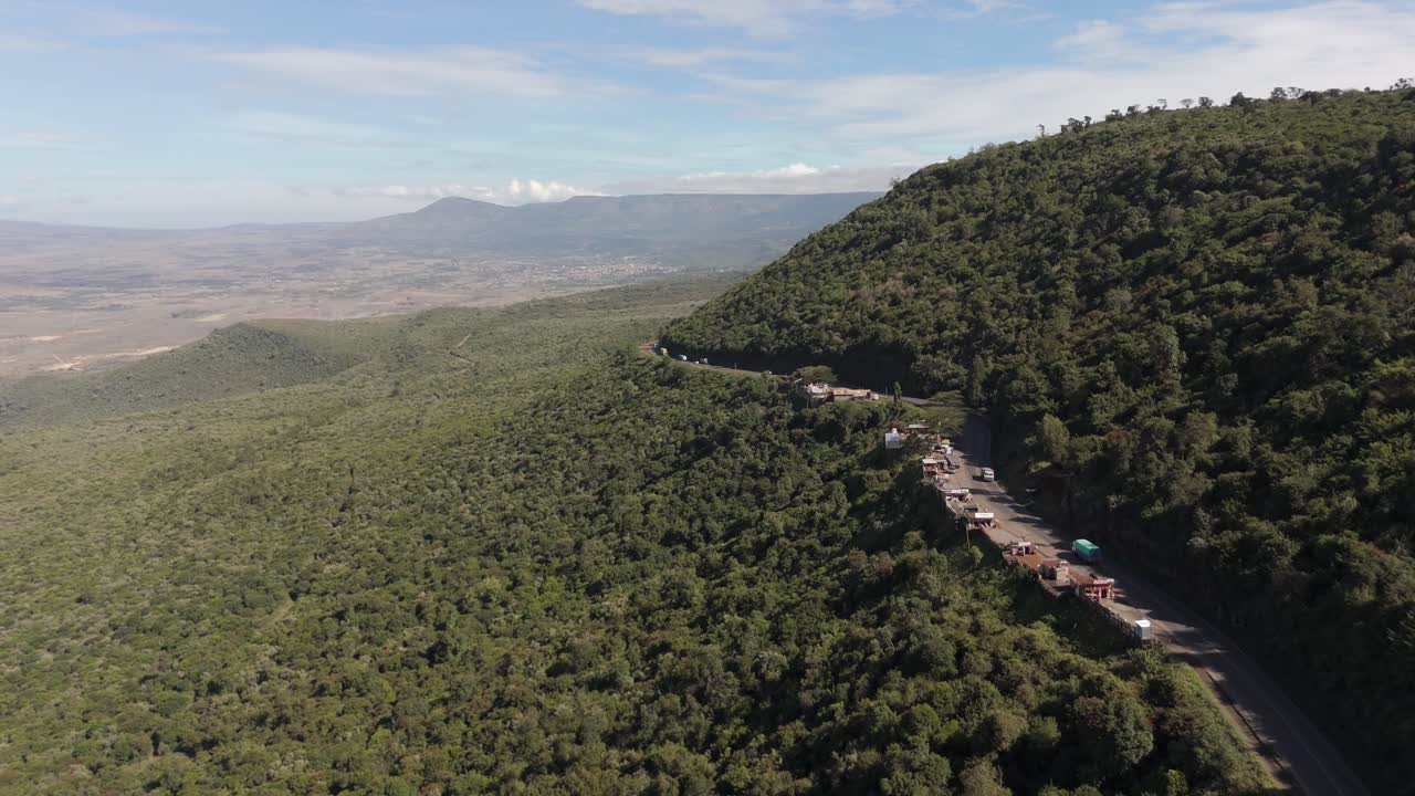 Panoramica aerea a sinistra su strada tortuosa attraverso la Great Rift Valley che mostra vasti paesaggi, verdi colline e veicoli che attraversano il Kenya