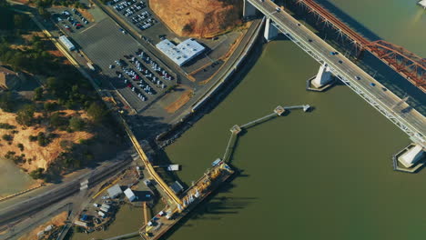 train moving at the waterfront of california bay under martinez bridge. industrial area with docks and big parking lots. top view.