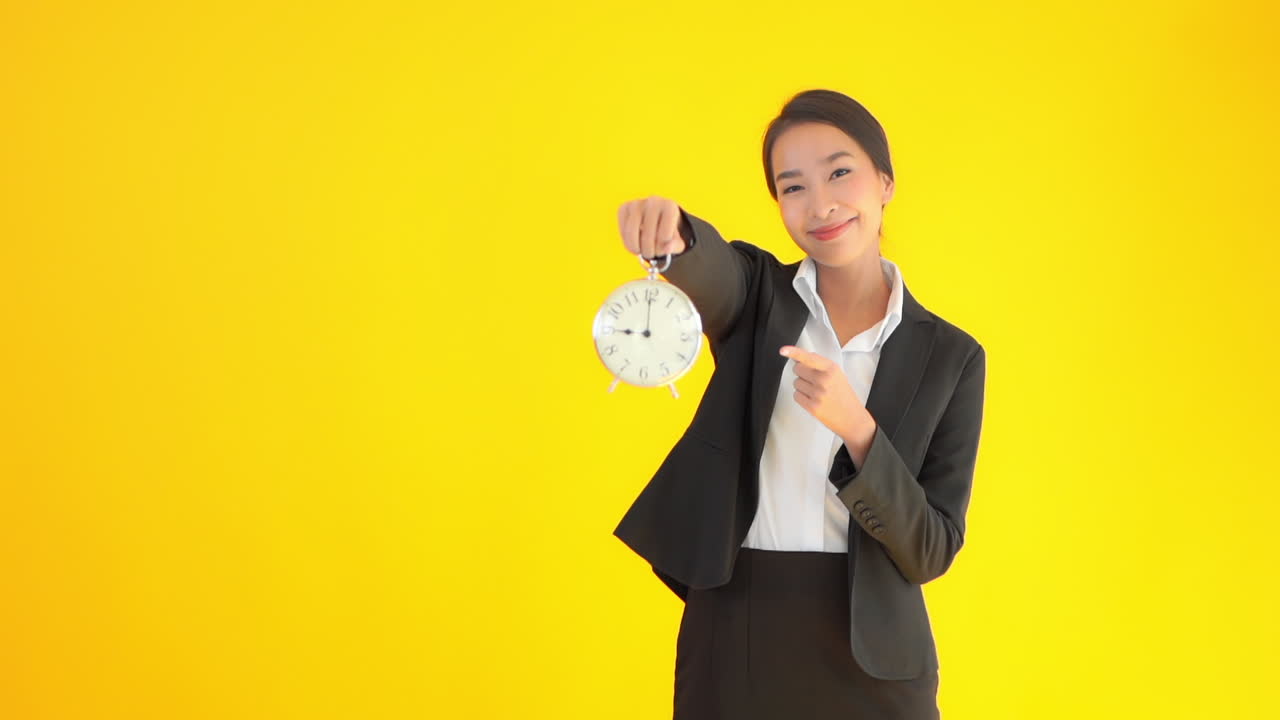 A young businesswoman lifts up a large clock smiles then points to the time. copy space