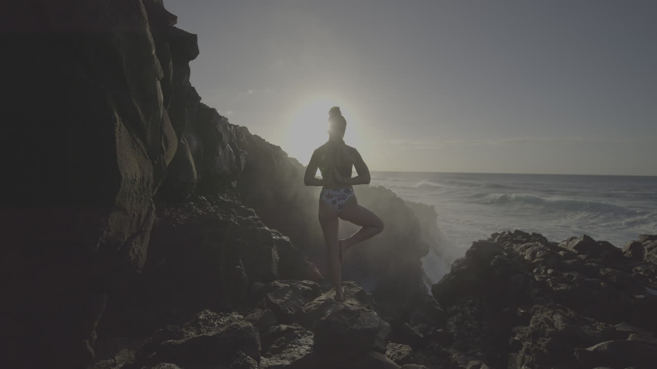 Woman practicing yoga by the ocean at sunrise