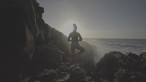 woman practicing yoga by the ocean at sunrise