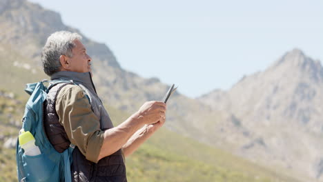 senior biracial man in mountains using tablet, in slow motion