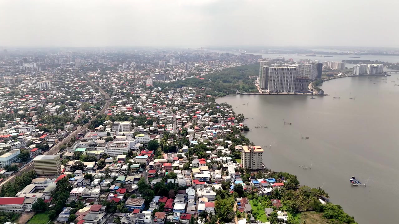 Pemandangan udara sinematik Ayyappankavu menampilkan lanskap kota tepi air yang semarak, lengkap dengan lingkungan perumahan padat, perairan pedalaman yang luas, dan menara-menara tinggi modern yang menjulang di sepanjang garis pantai.