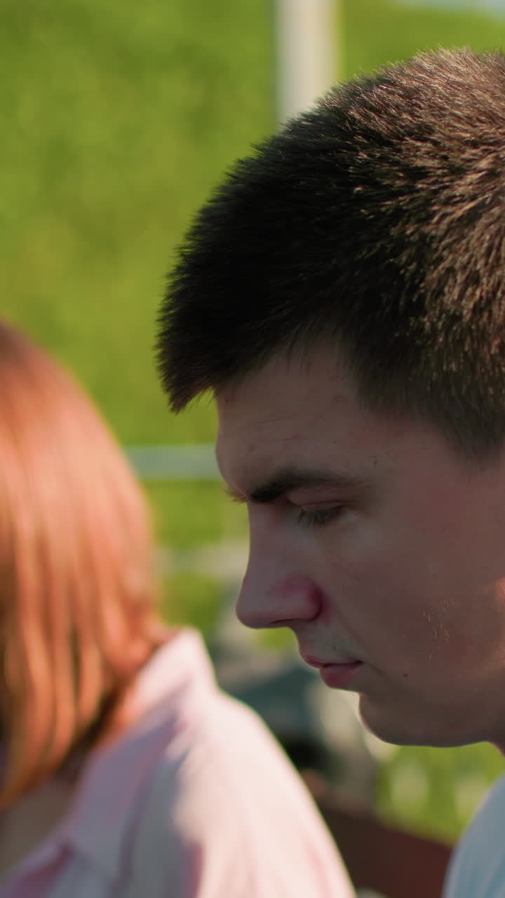 뒷면에서 약간 흐릿하게 보이는 친구를 으로 바라보는 젊은 남자의 클로즈업, 그에게 무언가를 보여주는, 나무, 철 레일링, 그리고 울창한 언덕으로 조용한 공원 설정