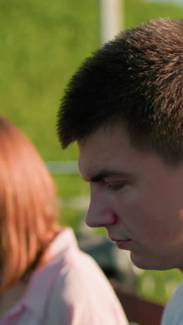 primer plano de un joven mirando a un amigo ligeramente borroso en el fondo que le está mostrando algo, un parque sereno con árboles, barandillas de hierro y colina exuberante