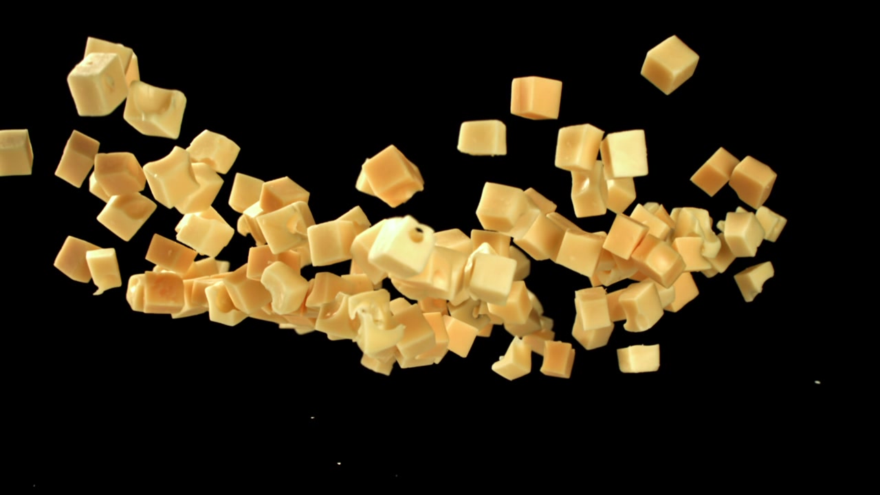 Movimento rallentato di cubetti di formaggio che cadono e galleggiano su sfondo nero