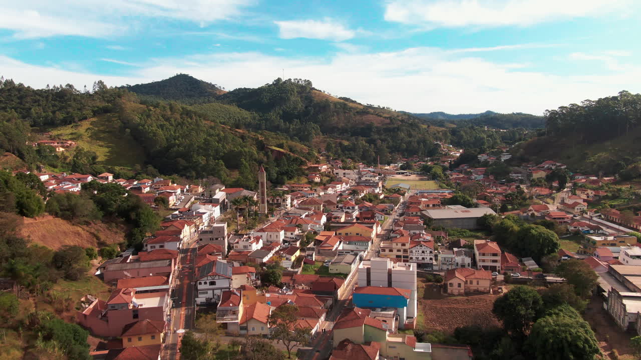 Aerial view of Delfim Moreira, Minas Gerais, Brazil, depicting a charming town nestled in a valley with rolling hills and dense forests